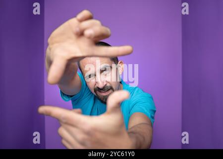 Young handsome man doing frame using hands palms and fingers, over purple background Stock Photo