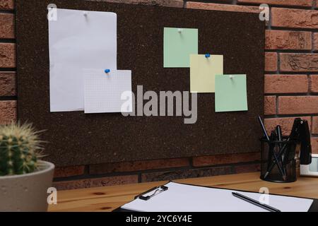 Corkboard with pinned notes hanging on brick wall over desk in office Stock Photo