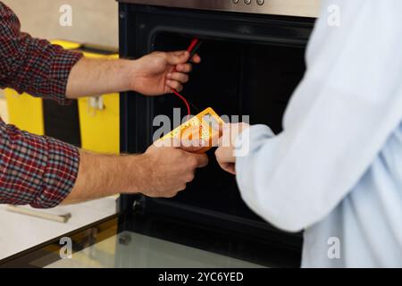 Repairman and woman testing oven element with multimeter, closeup Stock Photo