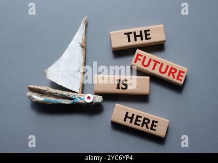 The future is here symbol. Concept words The future is here on wooden blocks. Beautiful grey background with boat. Business and The future is here con Stock Photo