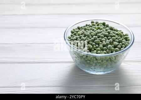 Frozen green peas in glass bowl on white wooden table, space for text Stock Photo