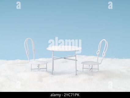 Winter composition made with white table and chairs covered with snow against blue background. Minimal winter concept. Stock Photo