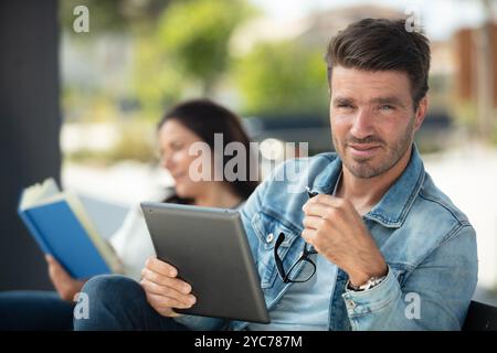 people at bus stop looking at book and tablet Stock Photo