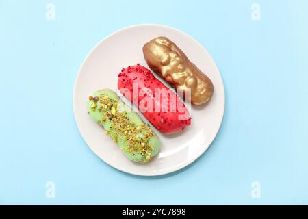 Plate with tasty glazed eclairs on color background Stock Photo