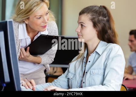mature female teacher helping adolescent student using computer Stock Photo