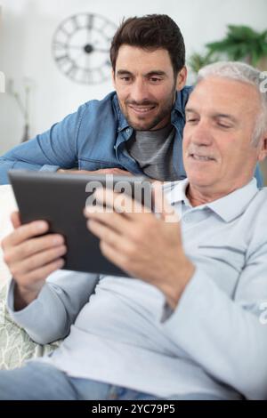 son teaching retiree dad to use banking app on tablet Stock Photo