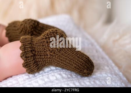 A pair of soft, brown knitted baby booties rests comfortably on a textured white blanket, showcasing intricate patterns and a warm, inviting feel with Stock Photo