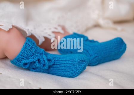 A pair of vibrant blue knitted baby booties rests on a plush white blanket adorned with delicate lace. The soft texture adds warmth and comfort to the Stock Photo