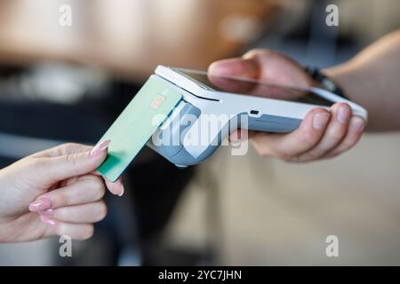 Customer paying with credit card using POS machine indoors, closeup, Customer Uses Debit Card to Pay Through Bank Terminal Stock Photo