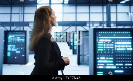 Engineer inspecting server room hardware, walking between supercomputers. IT professional supervising data center workplace, checking equipment, monitoring performance, camera A Stock Photo
