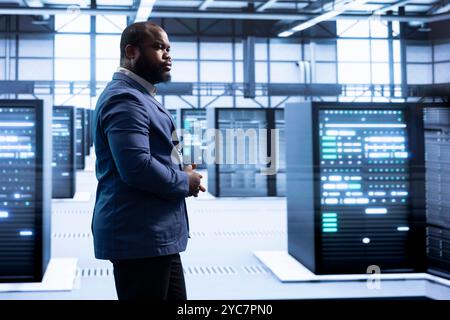 Supervisor overseeing server room, implementing and maintaining security measures, protecting systems from unauthorized access. Professional walks in data center workspace, doing hardware maintenance Stock Photo