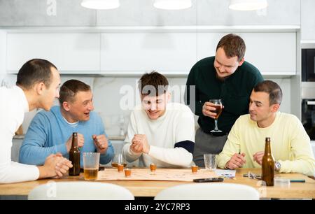 Group of cheerful men engaged in alcohol-fueled board game Stock Photo