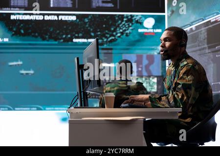 Military intelligence specialist using modern satellite systems and real time data to ensure national defense operations in a high tech control center base. Army professional working at computer. Stock Photo