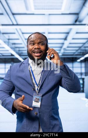 Manager talking on smartphone in high tech data center housing advanced computing gear. Specialist delegating tasks in technologically advanced server hub during telephone call Stock Photo