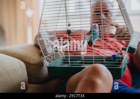 Elderly man enjoying time with pet bird in a cage at home Stock Photo