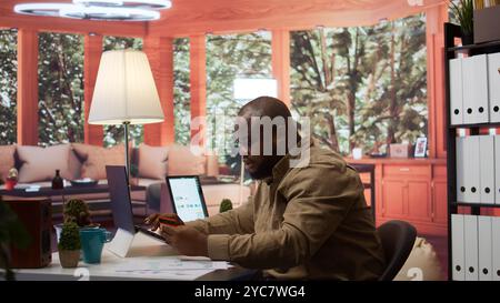 Business owner makes a payment with his card for online shopping at his home, electronic banking to buy resources for his startup. Entrepreneur purchasing something on laptop. Camera B. Stock Photo