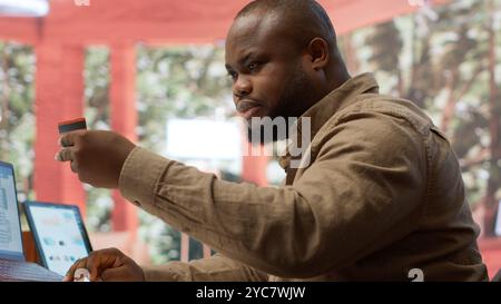 Entrepreneur using a card to make an online shopping payment via electronic banking, purchasing things to help the startup activity. Business owner makes a payment at his home office. Camera A. Stock Photo