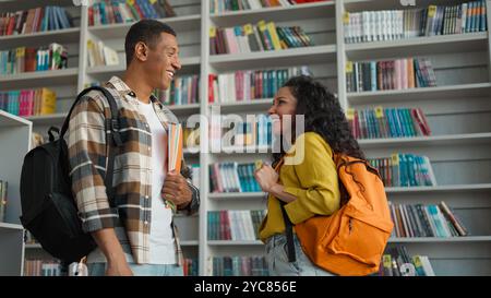 Two people African American man latin hispanic woman talking library reading club literature students bookstore bookshelves communication smiling Stock Photo