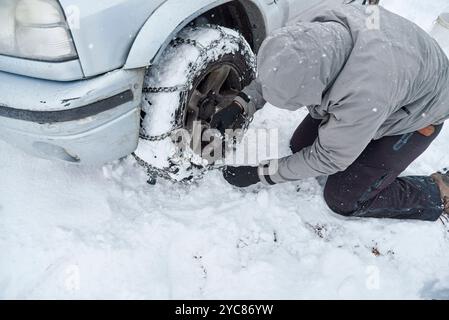 Travel in wintertime, unrecognizable man putting chains on the wheels of an SUV vehicle, in order to be able to move forward over the snow on a mounta Stock Photo