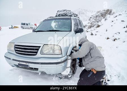 Travel in wintertime, unrecognizable man putting chains on the wheels of an SUV vehicle, in order to be able to move forward over the snow on a mounta Stock Photo