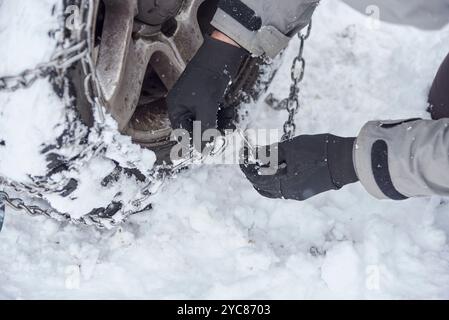 Travel in wintertime, close up view of the hands of an unrecognizable person putting chains on the wheels of an SUV vehicle, in order to be able to mo Stock Photo