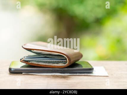 Brown leather wallet and smartphone paste on the wooden in blur background. Stock Photo