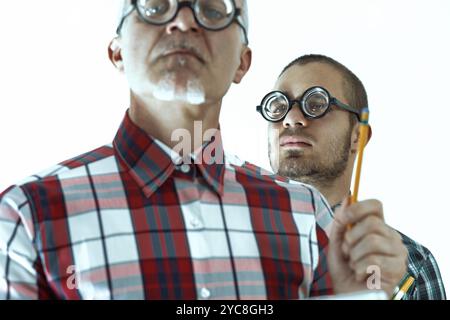 Two nerdy scientists with funny glasses are trying to find a solution to a scientific problem, deep in thought while holding pencils Stock Photo