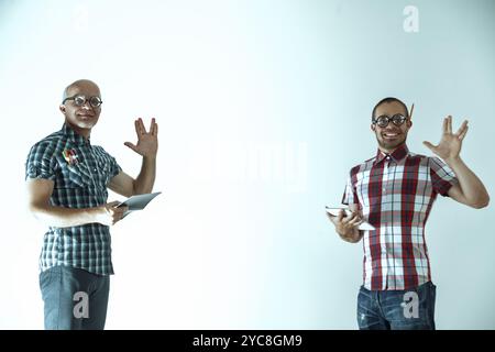 Two nerdy scientists are standing in their lab coats, holding tablets, and making hand gestures. They are excited about a new discovery Stock Photo