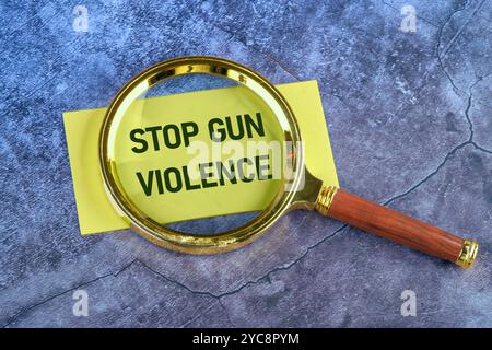 STOP GUN VIOLENCE text written on yellow paper through a magnifying glass on a blue abstract background, a conceptual photo. Stock Photo