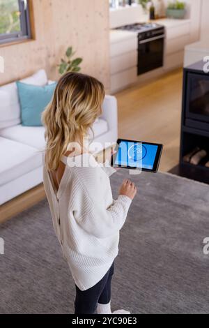 Christmas time, Woman adjusting smart thermostat on tablet in cozy living room, at home Stock Photo