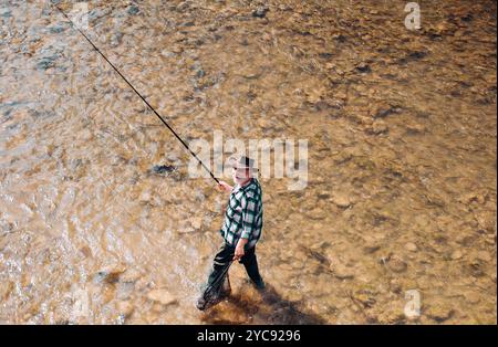 Mature man fishing on the pond. Happy fly fishing. Angler catching the fish. Master baiter. Catching and fishing. Rural getaway. Giving your hobby. Stock Photo