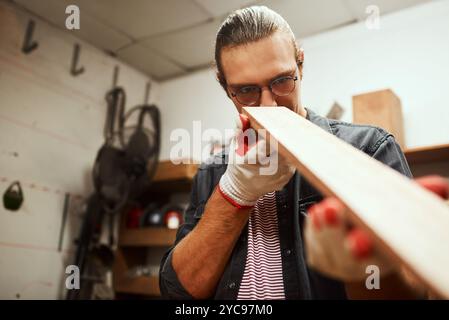 Man, carpenter or checking with wood at workshop for project or woodwork at manufacture. Precision, male person or designer with material, tools or Stock Photo