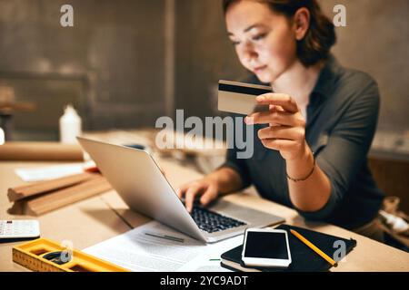 Credit card carpenter and woman in workshop, laptop and online shopping with payment for supplies. Person, entrepreneur and business owner with Stock Photo