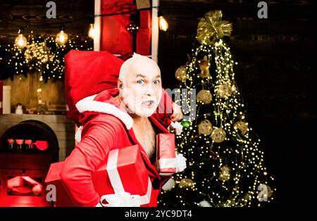 Burglar man dressed in Santa wearing a Santa hat. Thief Santa with bag on christmas background. Thief stole new years presents. Santa in the mask with Stock Photo