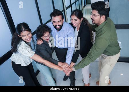 Group of five young indian business people joining hands together and celebrating team success. Team work, bonding, workplace concept. Stock Photo