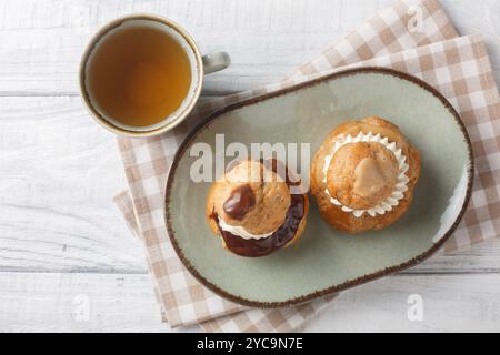 Exquisite Religieuse eclair pastry with patissiere cream with chocolate and coffee glaze close-up in a bowl on a wooden table. Horizontal top view fro Stock Photo