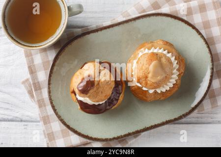 Religieuse French choux bun patisserie classic, filled with fluffy vanilla cream closeup on the plate on the wooden table. Horizontal top view from ab Stock Photo