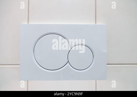 Economic white dual buttons of flush toilet bowl on tiled wall in bathroom. Flushing system in closet Stock Photo