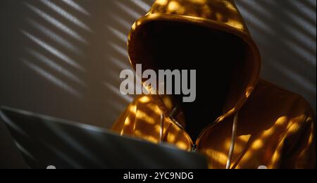 Computer hacker wearing yellow hoodie using laptop, selective focus Stock Photo