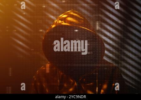 Unrecognizable computer hacker wearing yellow hooded jacket in dark room, hexadecimal code overlaying the image, selective focus Stock Photo