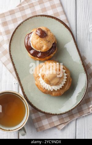 Religieuse pastry is composed of two choux buns filled with pastry cream, topped with chocolate ganache and decorated with cream closeup on the plate Stock Photo