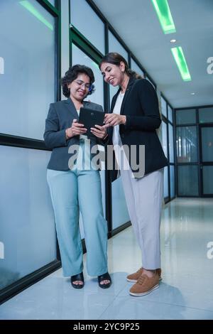 Two indian businesswoman consulting on new project holding digital tablet standing in office. workplace and corporate concept. Stock Photo
