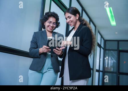 Two indian female entrepreneurs consulting on new project using digital tablet standing in office. workplace, business and corporate concept. Stock Photo