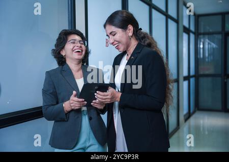 Two indian female business colleagues consulting on new project using digital tablet standing in office. workplace and wireless technology concept. Stock Photo