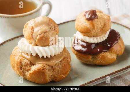 Religieuse French choux bun patisserie classic, filled with fluffy vanilla cream closeup on the plate on the wooden table. Horizontal Stock Photo