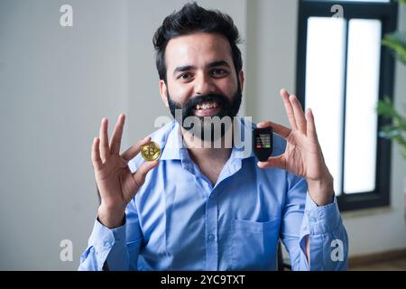 Young indian business man holding bitcoin and hardware wallet in hand, Investment and Security, Digital asset, Cryptocurrency. Stock Photo