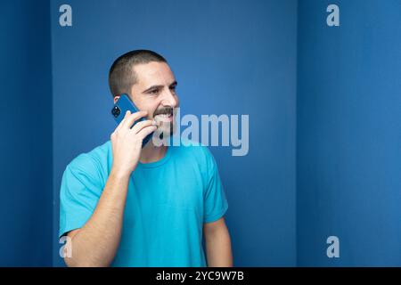 Cheerful young man in blue shirt and glasses, talking on the phone and laughing to friend's joke Stock Photo