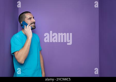 Cheerful young man in blue shirt speaking on the phone and laughing to friend's joke Stock Photo
