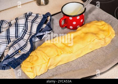 Pulled dough stuffed with sliced apple, red mug and checkerd towel on kitchen board. Preparation strudel. Stock Photo