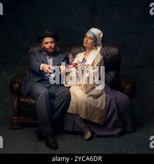 Couple in vintage European clothing playing video games, blending old-world fashion with modern entertainment in playful scene. Stock Photo
